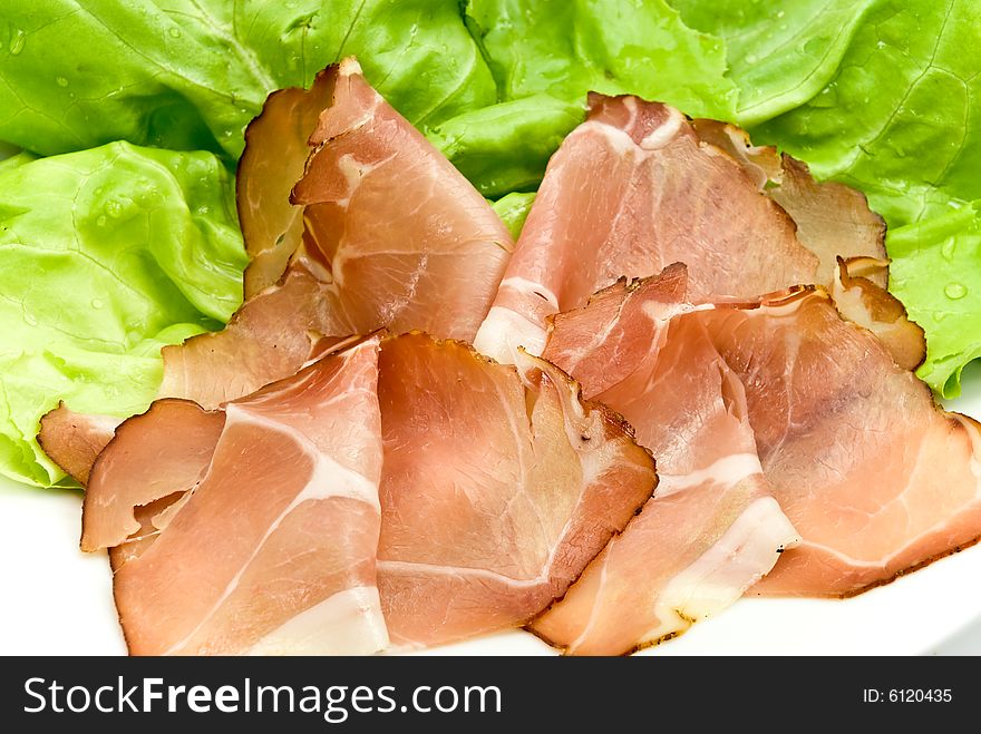 Many smoked slices of ham with salad.
