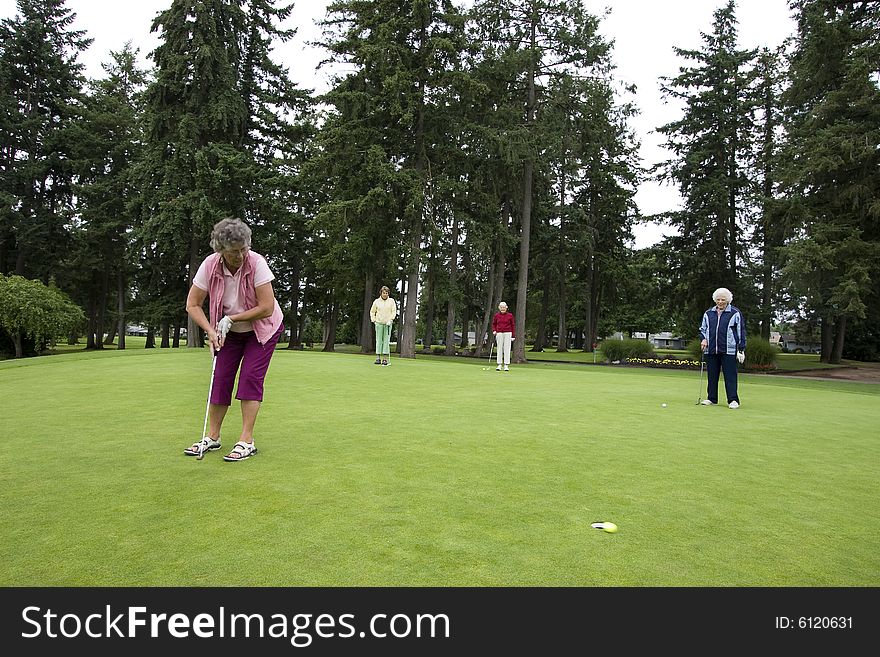 Elderly woman teeing off on the golf course as her three friends watch. Horizontally framed photo.