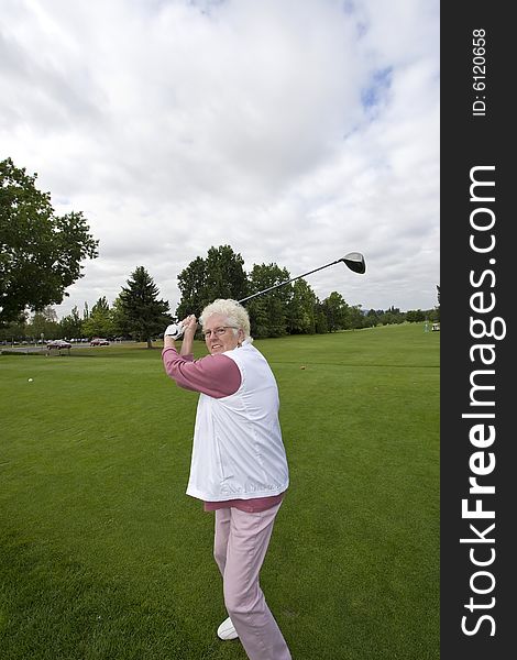 Elderly woman swinging a golf club. Vertically framed photo. Elderly woman swinging a golf club. Vertically framed photo.