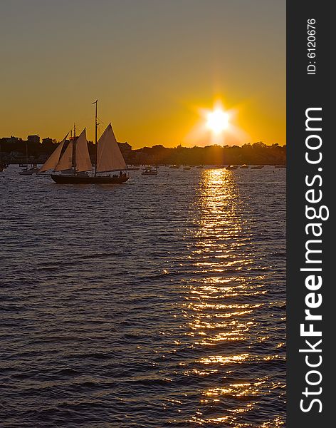 A sailboat drifting in harbor during sunset. A sailboat drifting in harbor during sunset.