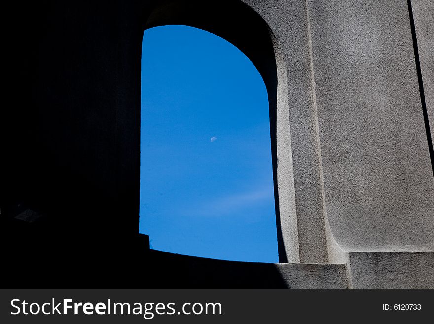 Stone arch, half in the shadow half in sunlight with blue sky and a day moon visible thru the opening. Stone arch, half in the shadow half in sunlight with blue sky and a day moon visible thru the opening.