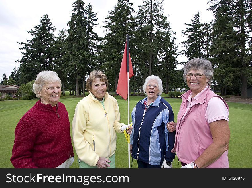 Four elderly woman smile as one holds a golf flag. Horizontally framed photo. Four elderly woman smile as one holds a golf flag. Horizontally framed photo.