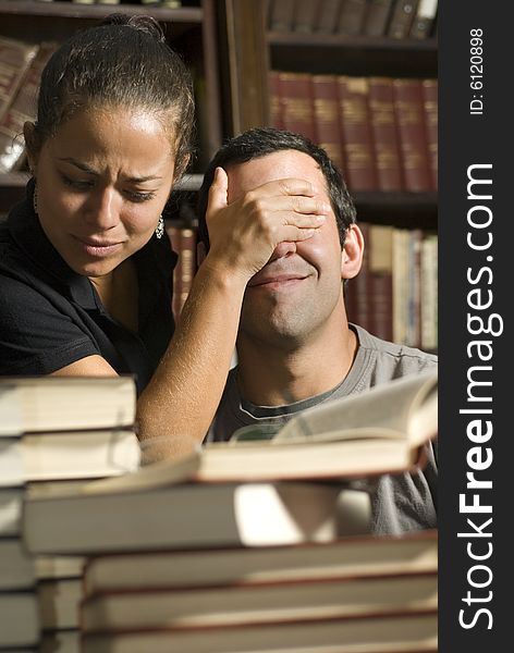Woman covers man's eyes while studying in library. Vertically framed photo. Woman covers man's eyes while studying in library. Vertically framed photo.