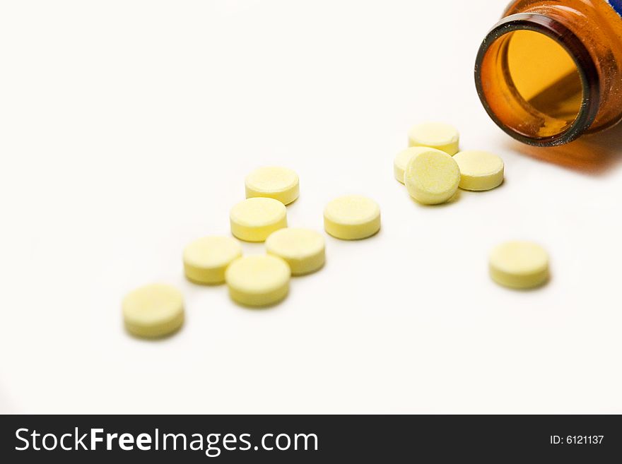 A few yellow pills and container, isolated over white background