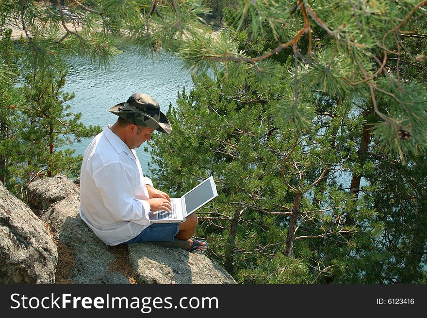 Man working on a laptop on the rocks. With copy space - you can place what you wish on the monitor. Man working on a laptop on the rocks. With copy space - you can place what you wish on the monitor.