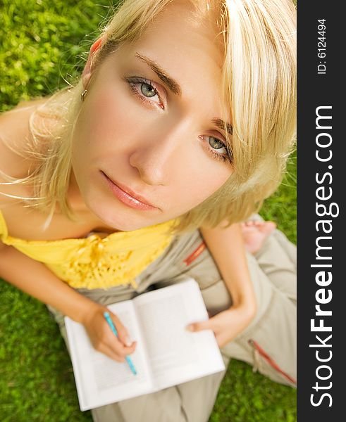 Sad young girl sitting oudoors on a grass and reading book