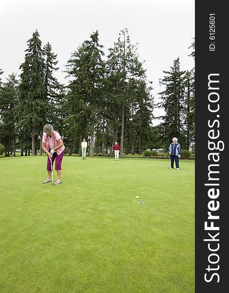 Elderly woman teeing off on the golf course as her three friends watch. Vertically framed photo.