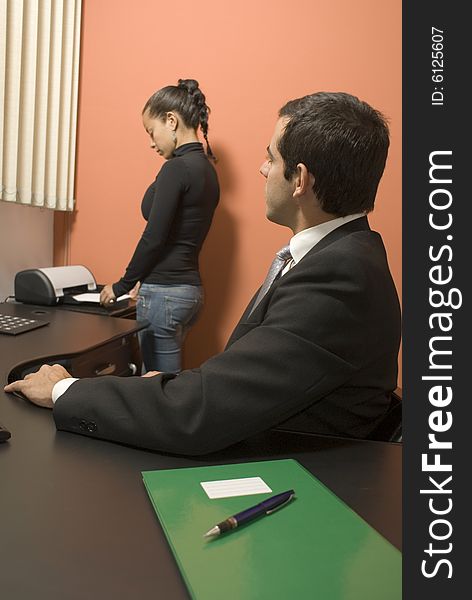 Businessman watches his secretary use the fax machine while sitting at his desk. Vertically framed photo. Businessman watches his secretary use the fax machine while sitting at his desk. Vertically framed photo.