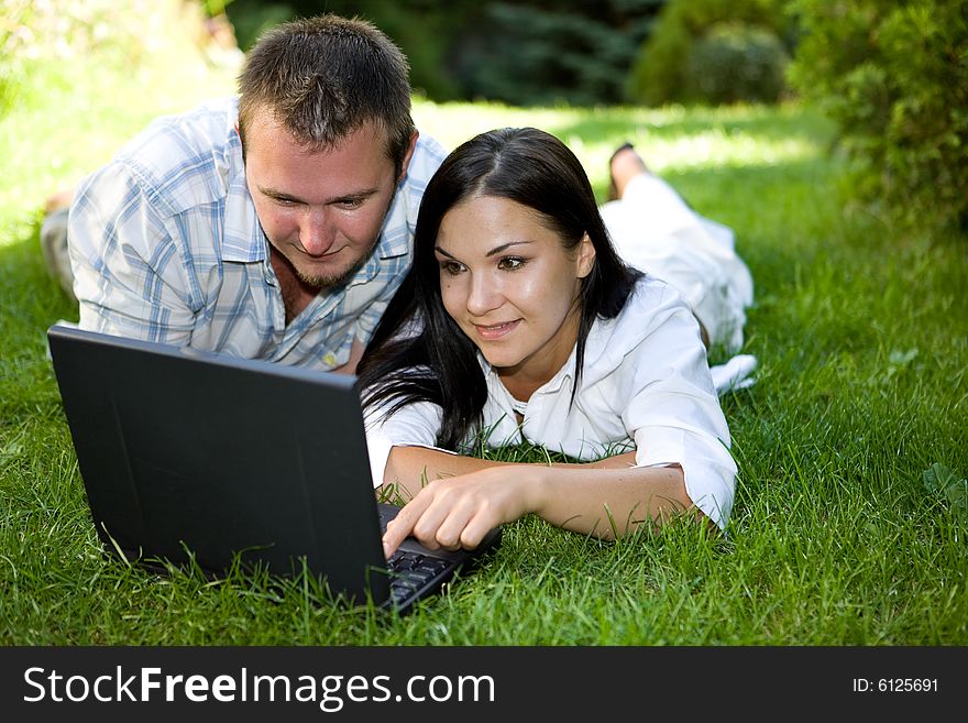 Couple lying on grass with laptop. Couple lying on grass with laptop