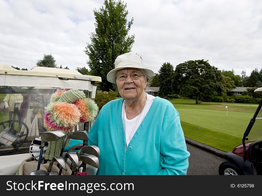 Female elderly woman puts golf club in golf cart. Horizontally framed photo. Female elderly woman puts golf club in golf cart. Horizontally framed photo.