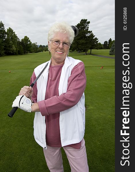 Elderly golfer holding her golf club and smiling. Vertically framed photo.