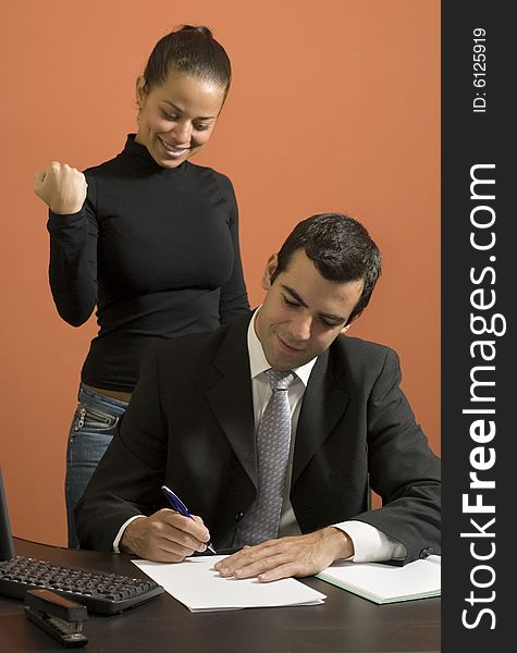 Businessman working at his desk while his secretary stands behind him pretending to be angry. Vertically framed photo. Businessman working at his desk while his secretary stands behind him pretending to be angry. Vertically framed photo.