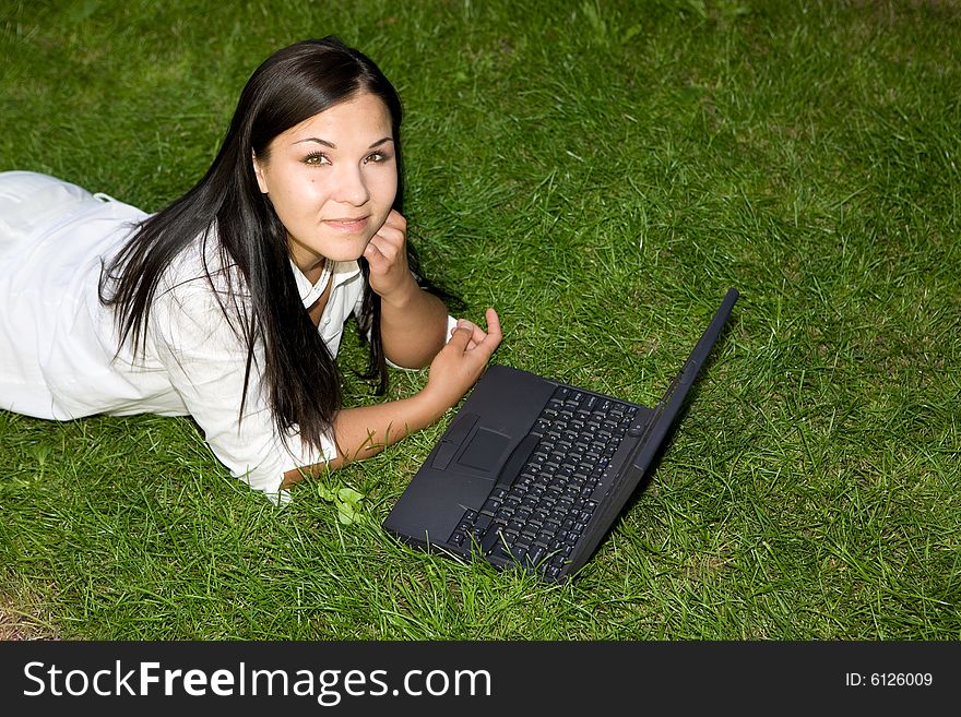 Happy brunette woman lying on grass with laptop. Happy brunette woman lying on grass with laptop