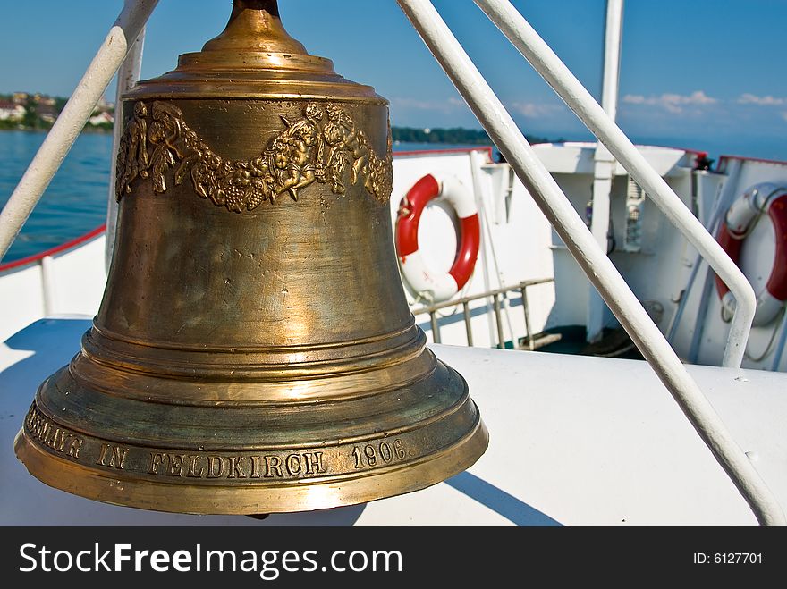 A golden ship's bell with the lake of constance in the background. A golden ship's bell with the lake of constance in the background