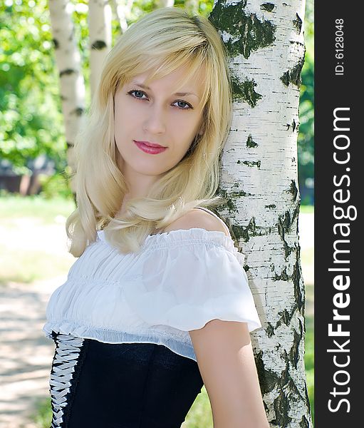 Portrait of pretty blonde girl near of birch stem