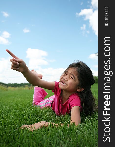 Little girl lying on grass in summer pointing up