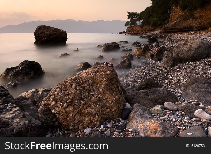 Image shows a rocky mediterranean seascape, photographed with a long exposure right after sunset.