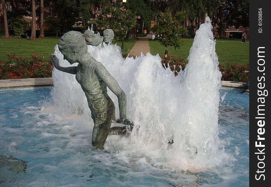 This is a water fountain that has bronze statues of people playing and having fun. This is a picture perfect college day. This is a water fountain that has bronze statues of people playing and having fun. This is a picture perfect college day.