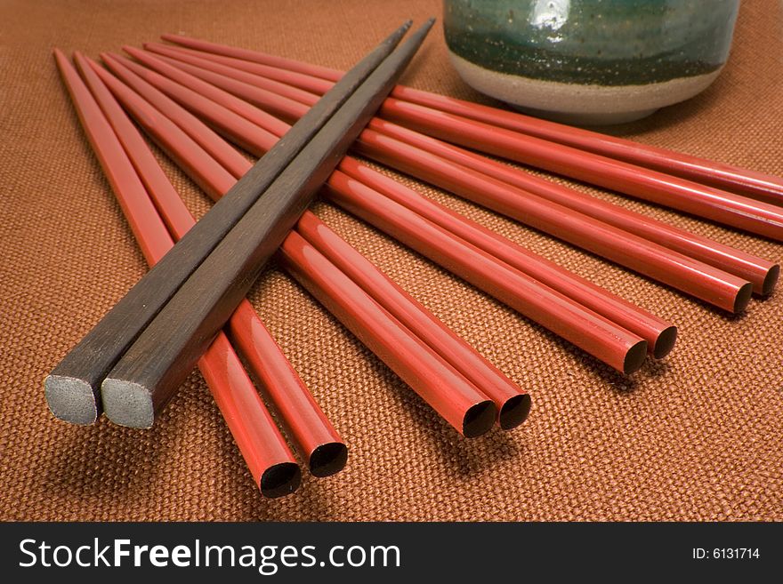 Red and brown chopsticks arranged diagonally leading to tea cup