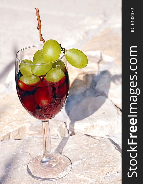 Red wine glass with grapes cluster over stone background. Red wine glass with grapes cluster over stone background