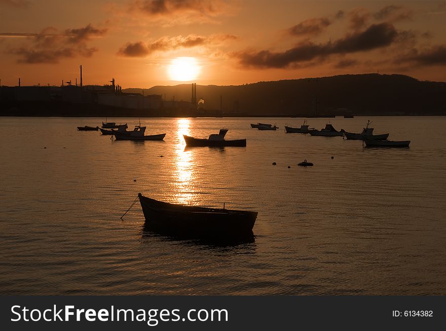 Some boats grounded on the sea. The light at the sunset produces  beautiful silhouettes of the boats and the factory in the background. Some boats grounded on the sea. The light at the sunset produces  beautiful silhouettes of the boats and the factory in the background.