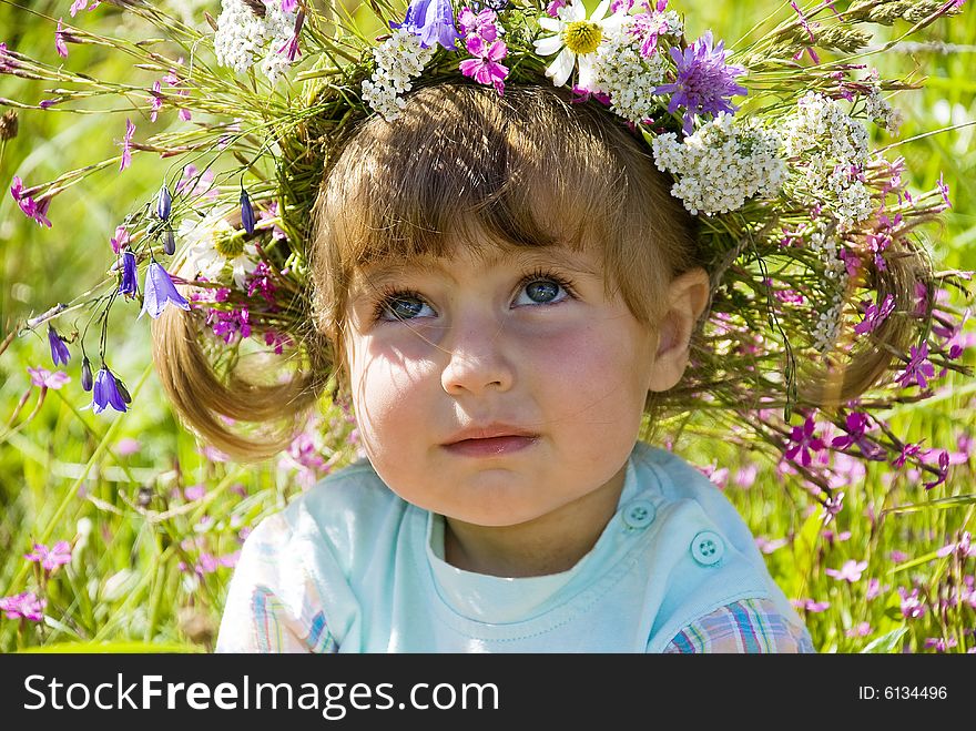 The little girl in wildflower diadem thoughtfully looks in the sky. The little girl in wildflower diadem thoughtfully looks in the sky.