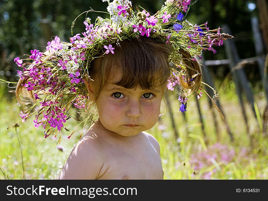 The little girl in wildflower diadem thoughtfully looks in the sky. The little girl in wildflower diadem thoughtfully looks in the sky.