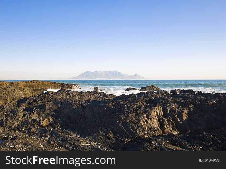 Table Mountain - the world famous landmark in Cape Town, South Africa. Picture taken on a clear Winters day from the Blouberg Strand beach. A rocky part of the beach is in the foreground. Table Mountain - the world famous landmark in Cape Town, South Africa. Picture taken on a clear Winters day from the Blouberg Strand beach. A rocky part of the beach is in the foreground.