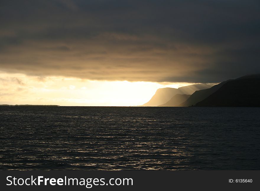 Golden cloudy sunset in a fjord with the clouds ending at the fjords mouth and the sun shining from behind them. Golden cloudy sunset in a fjord with the clouds ending at the fjords mouth and the sun shining from behind them.