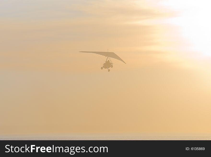 The faded silhouette of a motorized glider, disappearing into the sunset. The faded silhouette of a motorized glider, disappearing into the sunset.