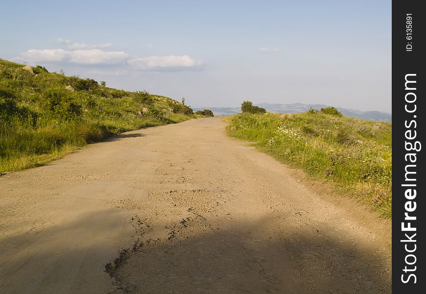 Dirty rural road, green meadow, blue sky. Dirty rural road, green meadow, blue sky.