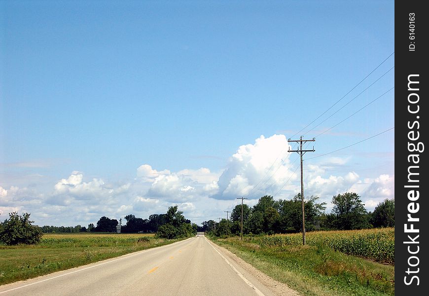 Country road with telephone pole, blue sky and clouds