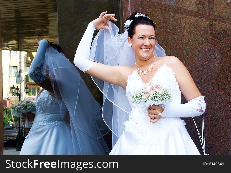 Cheerful bride holding her veil outdoor