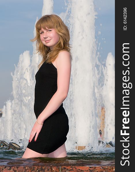 Beautiful girl in a black dress stands in a fountain