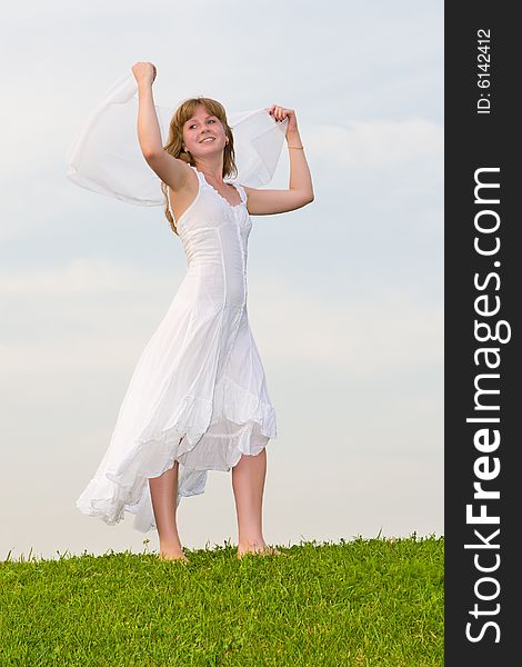 Girl with a white scarf in a hand stands on a green grass on a background of the blue sky. Girl with a white scarf in a hand stands on a green grass on a background of the blue sky