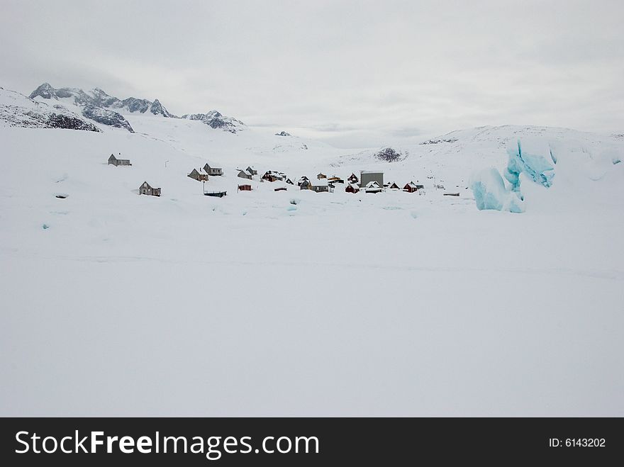 Inuit village and iceberg with mountains in background