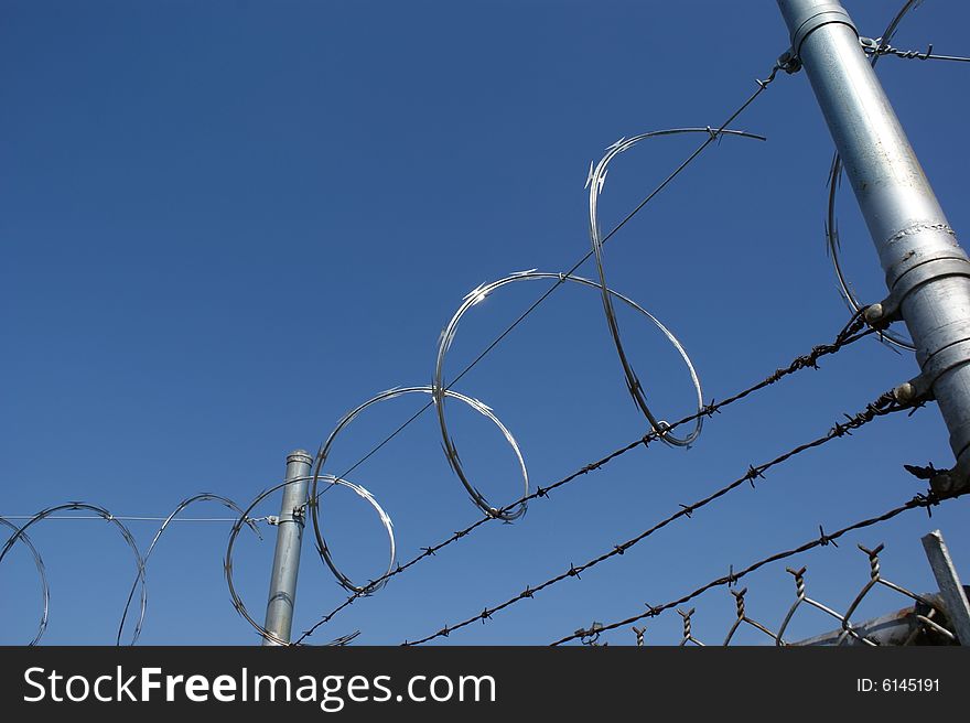 View of razor wire and barbed wire atop a fence.