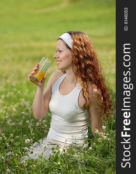 The girl sits on a background of a green lawn and drinks juice. The girl sits on a background of a green lawn and drinks juice