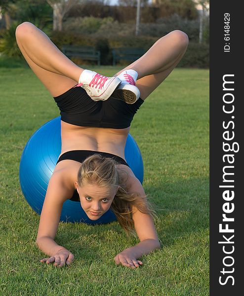 Young girl on blue fitness ball in the park.