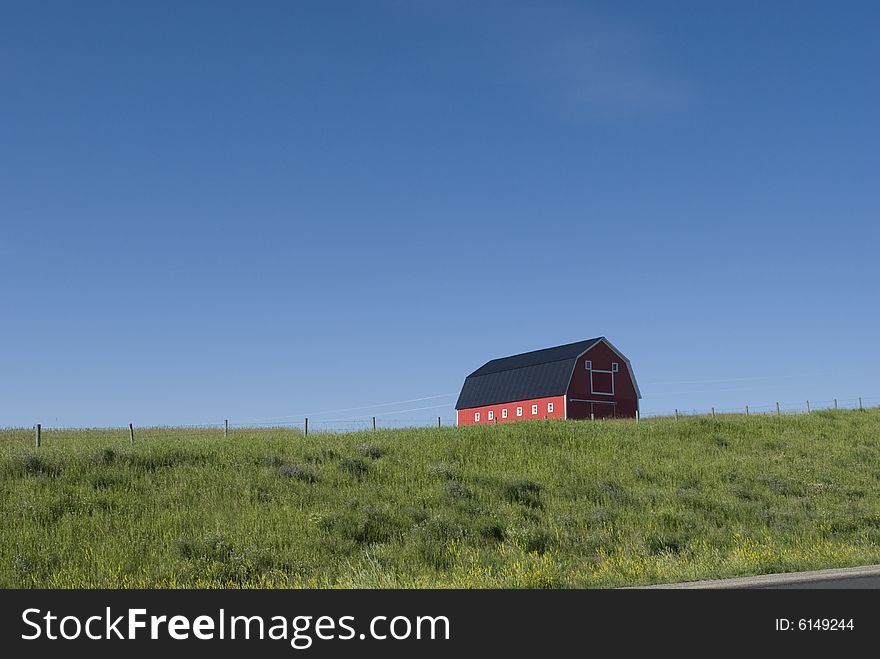 Scenic view of old red barn on green hillside with blue sky background. Scenic view of old red barn on green hillside with blue sky background.