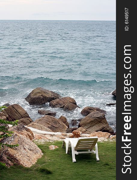 White deck chair overlooking the ocean with rocks on the shore.