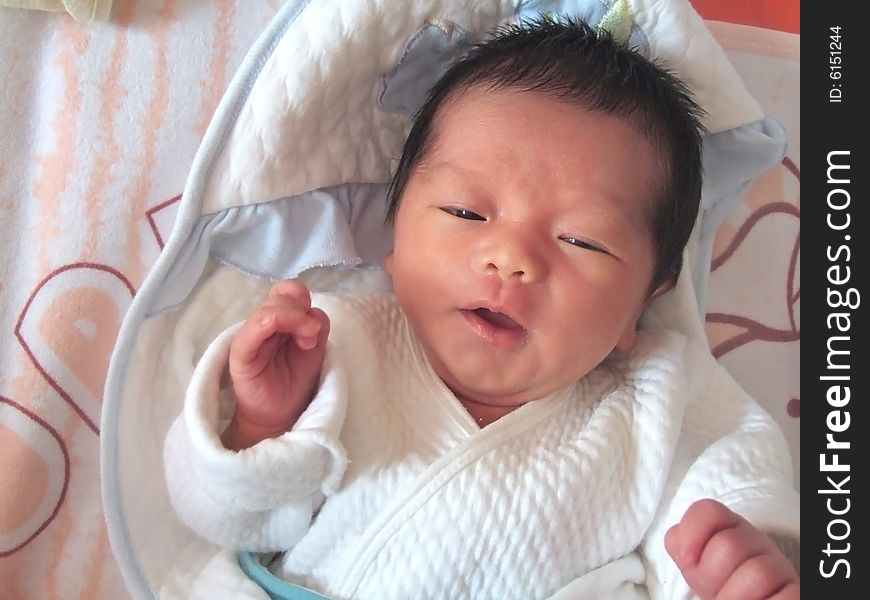 A Chinese baby is waving her hand on a bed. A Chinese baby is waving her hand on a bed