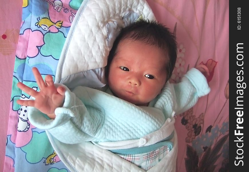 Lovely Baby in blue on a bed, making the gesture of 'OK'