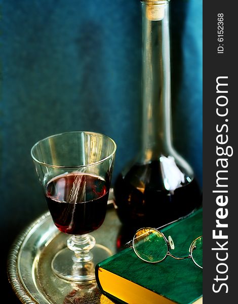 Bottle of red wine, glass,eyeglasses and book on a  silver tray. Bottle of red wine, glass,eyeglasses and book on a  silver tray