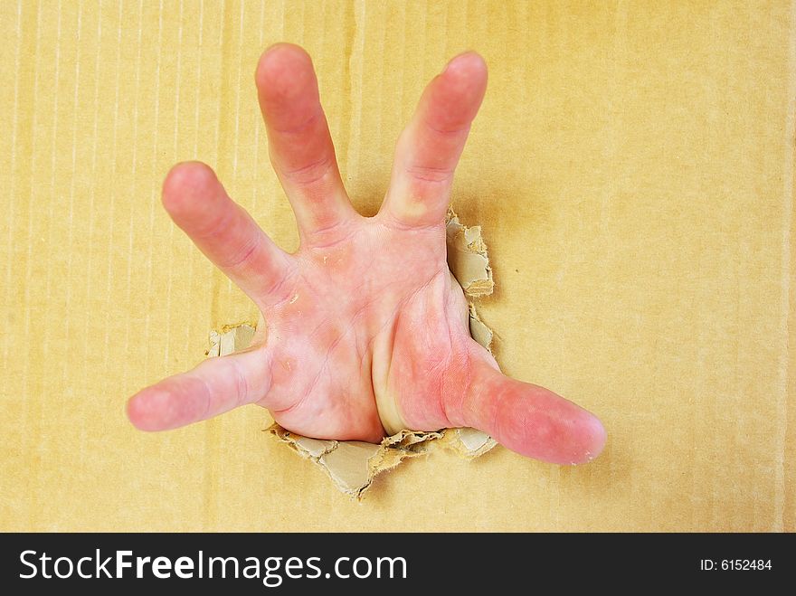 Hand opening a hole in brown cardboard