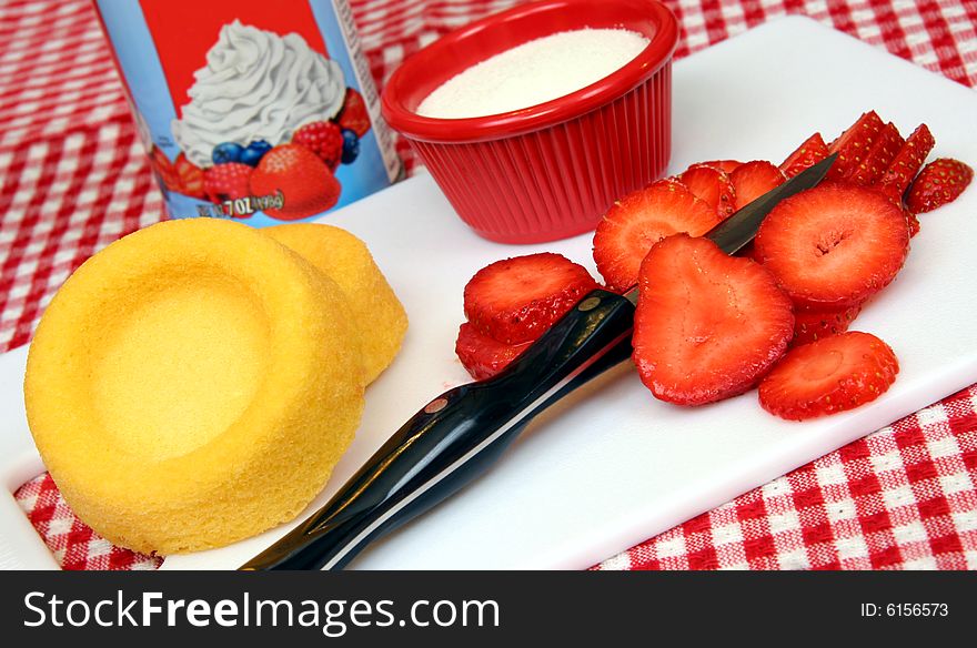 All ingredients on a white cutting board to make strawberry shortcakes, including fresh sliced strawberries. All ingredients on a white cutting board to make strawberry shortcakes, including fresh sliced strawberries.