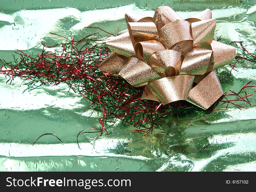Gold foil bow on green foil wrapping paper with red and green tinsel. Gold foil bow on green foil wrapping paper with red and green tinsel