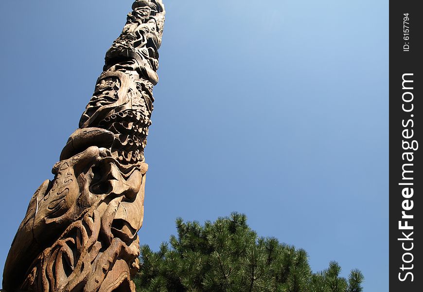 A Canadian Totem Pole with trees on a clear day.