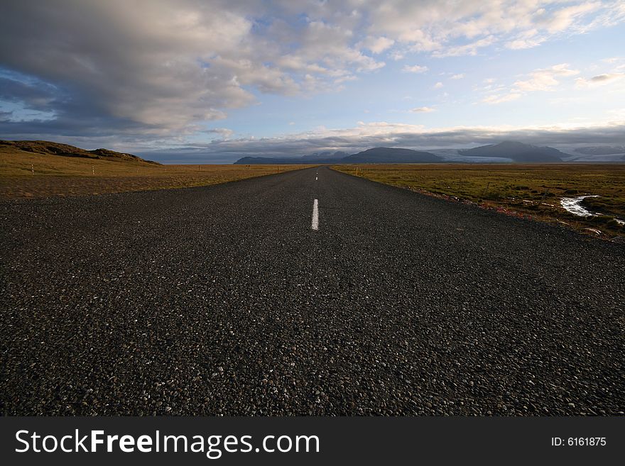 A wide angle perspective of a road disappearing towards the glaciers hiding in the distant mist. It's a photo of an empty A1 road that runs around the Iceland and passes lots of breathtaking scenery. A wide angle perspective of a road disappearing towards the glaciers hiding in the distant mist. It's a photo of an empty A1 road that runs around the Iceland and passes lots of breathtaking scenery.