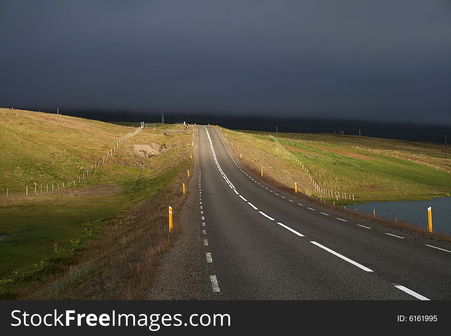 A road partially lit by sun with a dramatic background of stormy clouds. A road partially lit by sun with a dramatic background of stormy clouds.